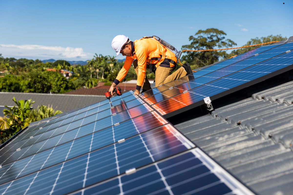 A man installing a solar panel on a roof, showcasing roofing services and renewable energy solutions.