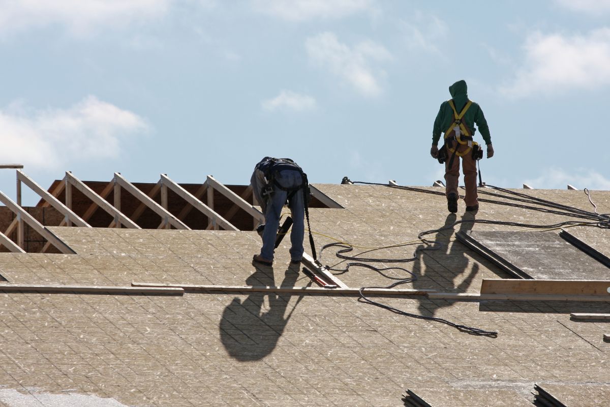 Two men inspecting and repairing blisters on the roof of a house. 