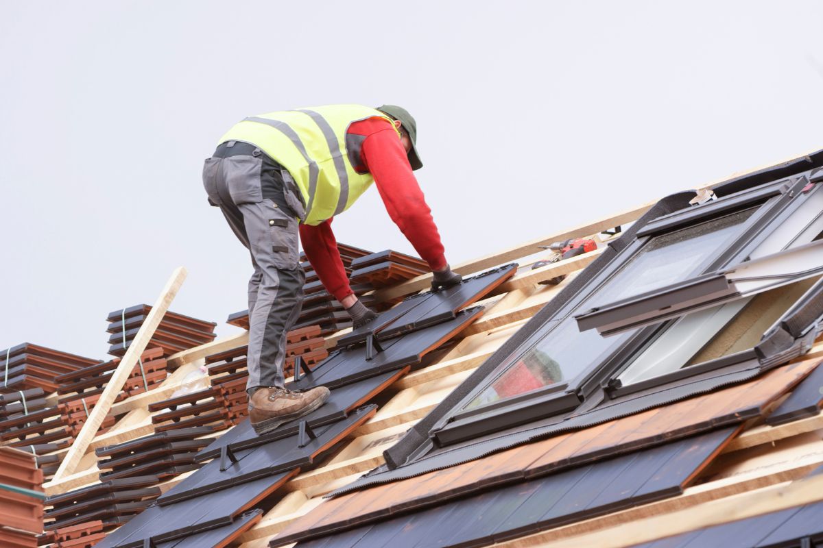 A man repairs a blistered roof while standing near a window, focusing on the task at hand.